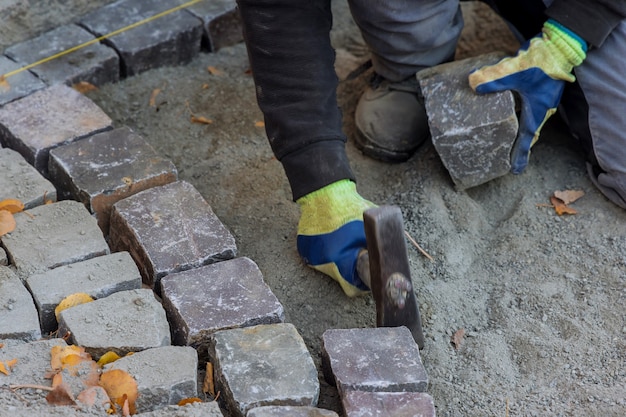 Pflasterarbeiter mit Hammerpflaster mit Granitsteinen Kopfsteinpflaster zum Pflastern der Straße