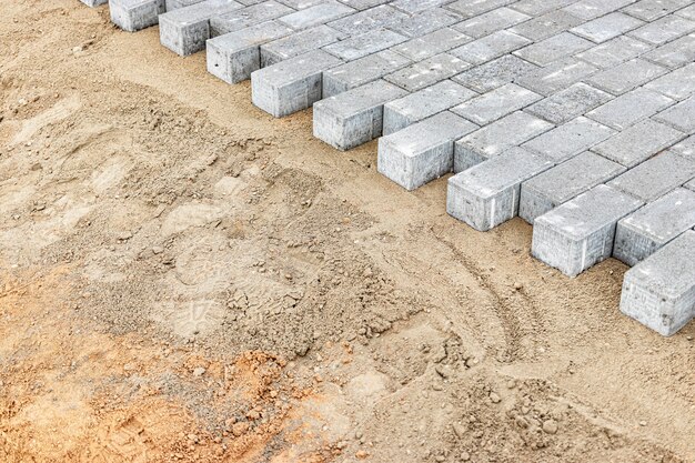 Pflasterreparaturen und Pflasterplatten auf der vorbereiteten Oberfläche, mit Fliesenwürfeln im Hintergrund. Verlegen von Gehwegplatten in der Fußgängerzone der Stadt. Pflastersteine und Bordsteine.