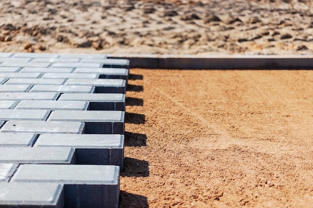 Pflasterreparaturen und Verlegung von Gehwegplatten auf der vorbereiteten Fläche mit Fliesenwürfeln im Hintergrund Verlegung von Gehwegplatten in der Fussgängerzone der Stadt Gehwegplatten und Bordsteine