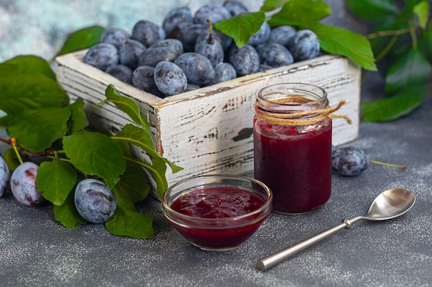 Pflaumenmarmelade in einem Glas. Im Hintergrund sind Pflaumen zu sehen. Tkemali-Sauce. Vorbereitung auf den Winter. Heller Hintergrund.