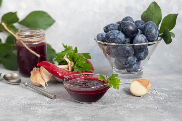 Pflaumenmarmelade in einem Glas. Im Hintergrund sind Pflaumen zu sehen. Tkemali-Sauce. Vorbereitung auf den Winter. Heller Hintergrund.