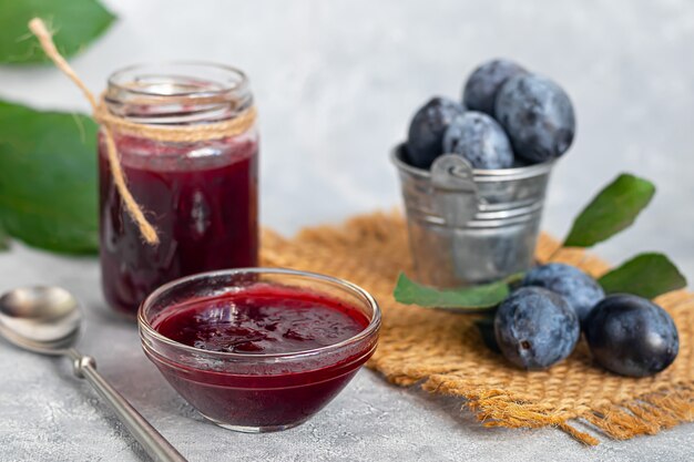 Pflaumenmarmelade in einem Glas. Im Hintergrund sind Pflaumen zu sehen. Tkemali-Sauce. Vorbereitung auf den Winter. Heller Hintergrund.