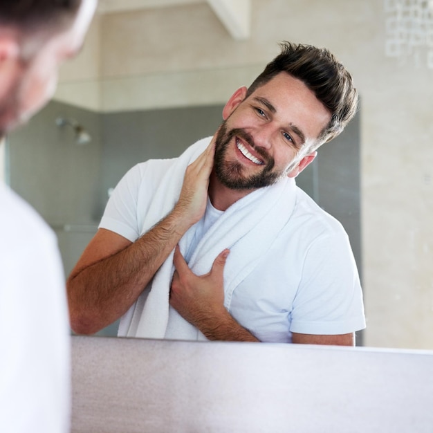 Pflegemorgen und Mann mit Reinigungs- und Spiegelroutine in einem Badezimmer mit einem Lächeln. Heimliche Reflexion und Hautpflege mit einem jungen Mann, der sich über Bartwuchs und Gesichtsdermatologie freut