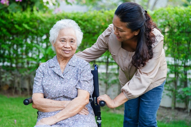 Pfleger helfen asiatischen älteren frauen mit behinderungen, die im medizinischen konzept des parks im rollstuhl sitzen