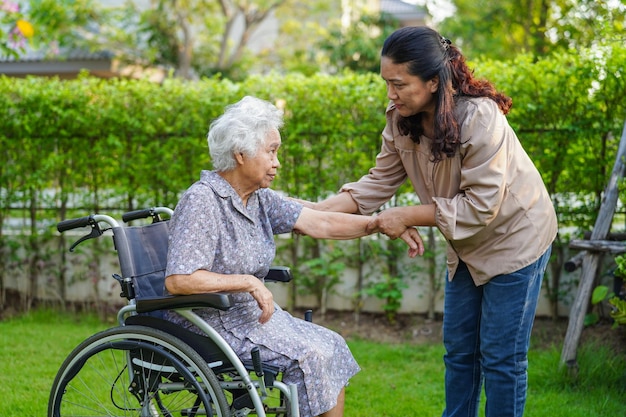 Pfleger helfen asiatischen älteren Frauen mit Behinderungen, die im medizinischen Konzept des Parks im Rollstuhl sitzen