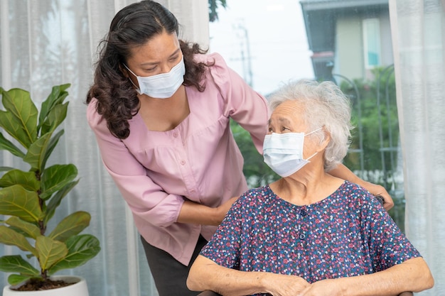 Pfleger helfen asiatischen Senioren oder älteren alten Damen, die im Rollstuhl sitzen und eine Gesichtsmaske tragen, um die Sicherheitsinfektion Covid19 Coronavirus zu schützen