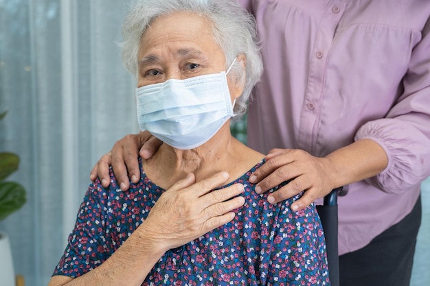 Pfleger helfen asiatischen Senioren oder älteren alten Damen, die im Rollstuhl sitzen und eine Gesichtsmaske tragen, um die Sicherheitsinfektion Covid19 Coronavirus zu schützen