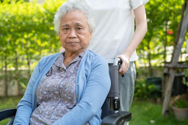 Pfleger helfen und pflegen Asiatische Seniorin oder ältere Patientin der alten Dame, die im Rollstuhl im Park sitzt, gesundes, starkes medizinisches Konzept