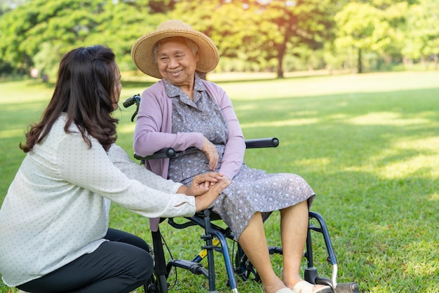 Pfleger helfen und pflegen Asiatische Seniorin oder ältere Patientin der alten Dame, die im Rollstuhl im Park sitzt, gesundes, starkes medizinisches Konzept