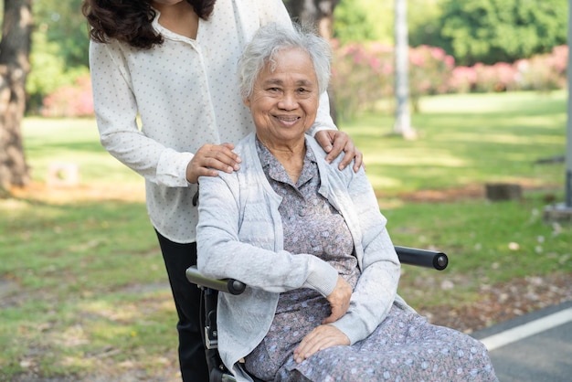 Pfleger helfen und pflegen Asiatische Seniorin oder ältere Patientin der alten Dame sitzt und freut sich im Rollstuhl im Park gesundes starkes medizinisches Konzept