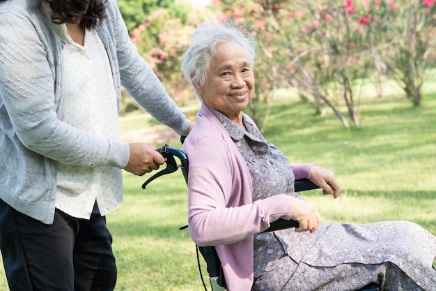 Pfleger helfen und pflegen Asiatische Seniorin oder ältere Patientin der alten Dame sitzt und freut sich im Rollstuhl im Park gesundes starkes medizinisches Konzept