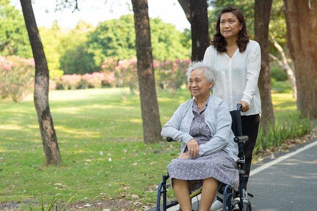 Pfleger helfen und pflegen Asiatische Seniorin oder ältere Patientin der alten Dame sitzt und freut sich im Rollstuhl im Park gesundes starkes medizinisches Konzept