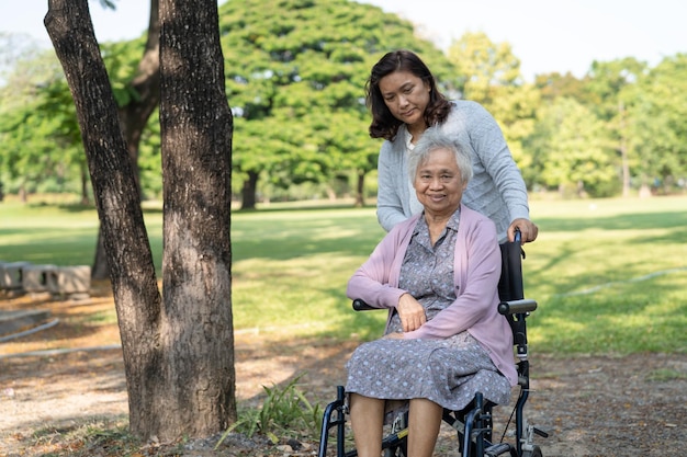 Pfleger helfen und pflegen Asiatische Seniorin oder ältere Patientin der alten Dame sitzt und freut sich im Rollstuhl im Park gesundes starkes medizinisches Konzept