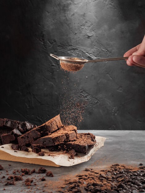Pfund Schokoladenkuchen, der auf einem grauen Tisch steht, der mit Kakao von einem Sieb bestreut wird.