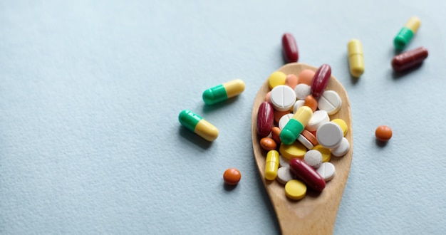Pharmazeutische Medizinpillen, Tabletten und Kapseln in einem Holzlöffel auf einem blauen Tisch.