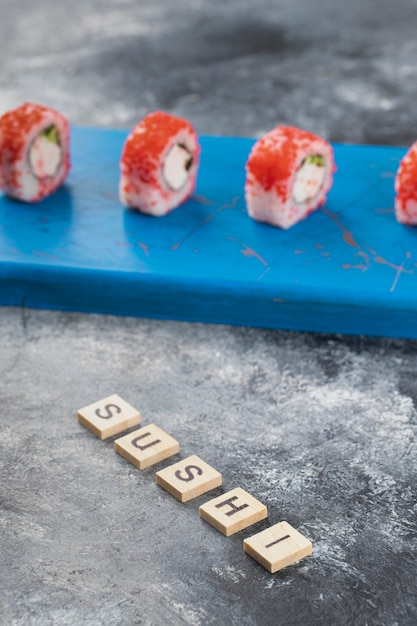 Philadelphia Roll mit frischem Lachs, Gurke, Frischkäse und Holzbuchstaben.