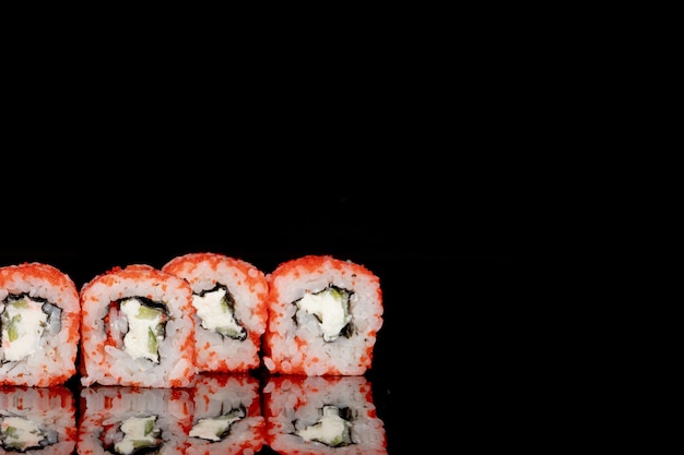 Philadelphia roll con salmón, queso y pepino sobre un fondo negro con reflejo. Sushi Filadelfia
