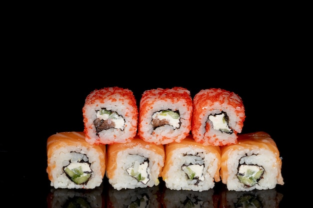 Philadelphia roll con salmón, queso y pepino sobre un fondo negro con reflejo. Sushi Philadelphia