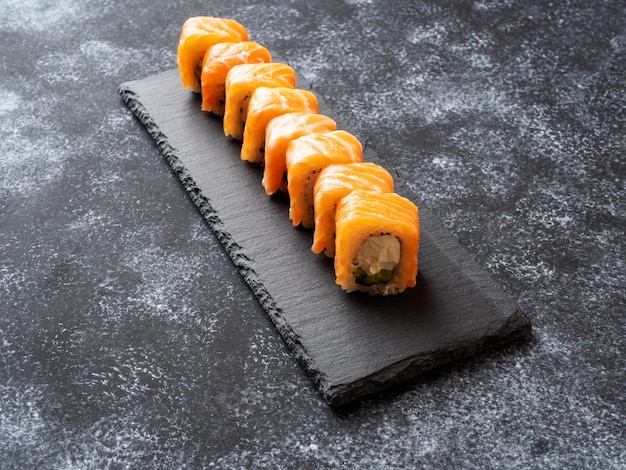 Philadelphia-Rollen, die auf einem Servierbrett aus Schiefer liegen Sushi-Set mit Lachs-Avocado-Frischkäse