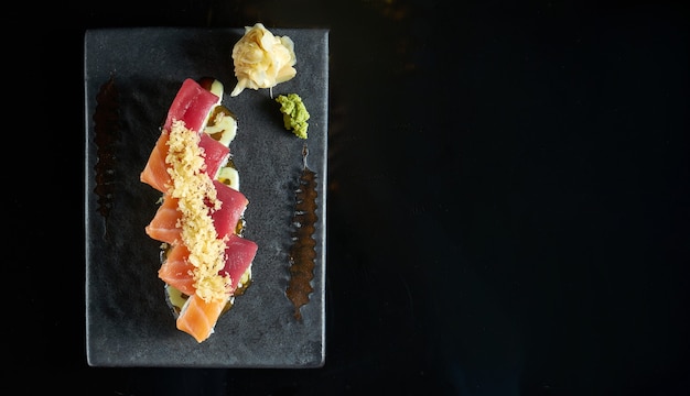 Philadelphia Sushi Roll mit Lachs und Thunfisch Krabbe, Avocado, serviert auf einem dunklen Teller mit Wasabi und Ingwer. Isolation auf einem schwarzen Tisch. japanisches Essen