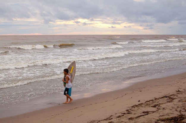 Philippinisches Kind mit Surfbrett am Strand