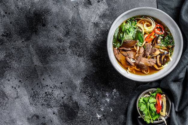 Pho Bo Sopa de fideos de arroz fresco vietnamita con carne de res, hierbas y chile. Fondo negro. Vista superior. Copia espacio