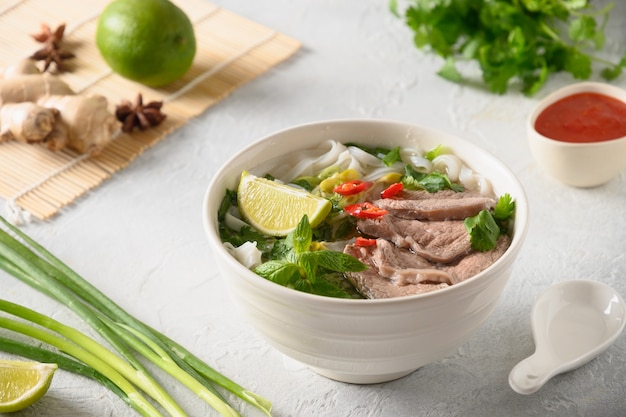 Pho Bo Suppe mit Rindfleisch in weißer Schüssel auf hellem Hintergrund vietnamesische Küche