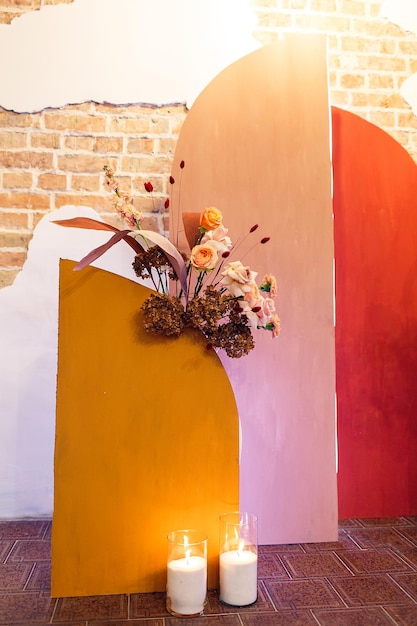 Photozone: arco de madera pintado en colores cálidos con flores sobre fondo de pared de ladrillo.