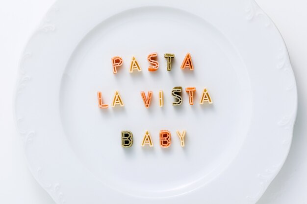 Phrase PASTA LA VIASTA BABY aus trockenen mehrfarbigen Nudeln auf einem weißen Teller.