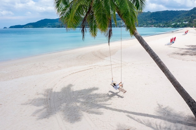 Phuket Tailandia Paraíso de playa tropical con columpio en la playa con una chica con camisa blanca Las mujeres se relajan en un columpio bajo una palmera de coco en una hermosa playa tropical Arena blanca