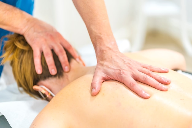 Physiotherapeut, der eine Massage mit einer Hand auf dem Rücken eines Mädchens mit einer Maske durchführt. Physiotherapeutische Sicherheitsmaßnahmen bei der Covid-19-Pandemie. Osteopathie, therapeutische Chiromassage