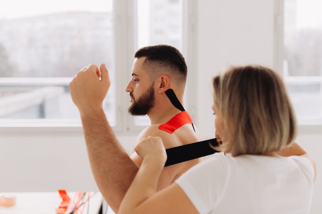 Physiotherapeut, der Kinesio Tape auf verletzte Schulterpatienten anbringt