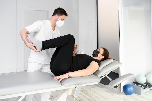 Physiotherapeut mit Schutzmaske, die einem Patienten eine Massage gibt. Wiedereröffnung mit physiotherapeutischen Sicherheitsmaßnahmen bei der Covid-19-Pandemie. Osteopathie, therapeutische Chiromassage.