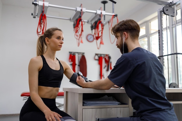 Physiotherapeutin misst den Blutdruck einer jungen sportlichen Frau