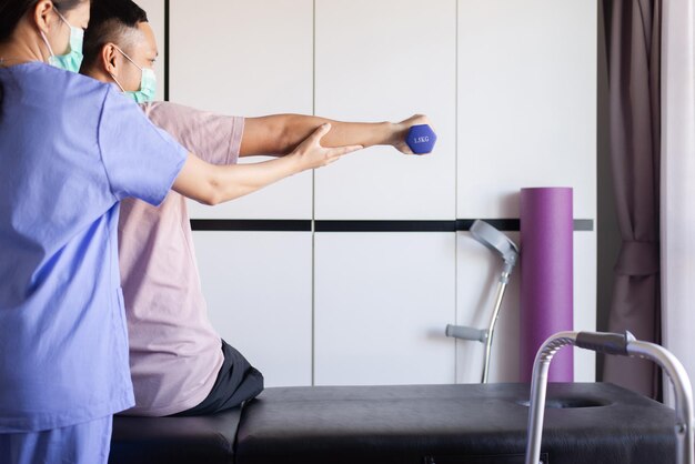 Physiotherapeutin trainiert mit Mannpatienten mit Hanteln in der Klinik, Konzept der körperlichen Therapie