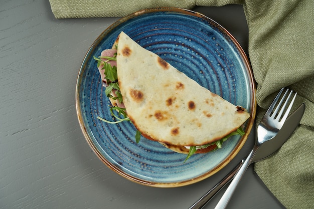 Piadina - klassisches italienisches Tortillabrot mit Vitello Tonato Kalbfleisch, Rucola, Mozzarella und Tomaten auf einem blauen Teller auf Holztisch. Schnelles Sandwich. Draufsicht, Kopierraum, flache Lage