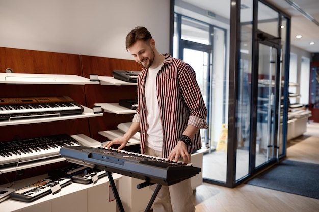 Pianista de homem jovem hipster tocando na loja de música tocando melodia de harmonia no piano elétrico. Mercado popular de instrumentos musicais