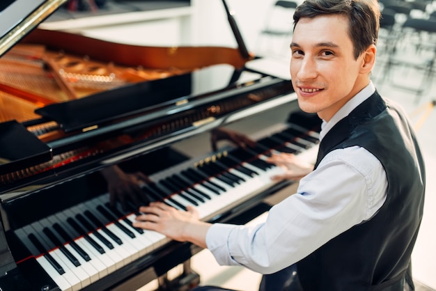 Pianista masculino posa ao piano de cauda preto