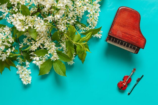 Piano y violín en miniatura con ramas de cerezo silvestre en flor. Vista superior, primer plano sobre fondo azul claro