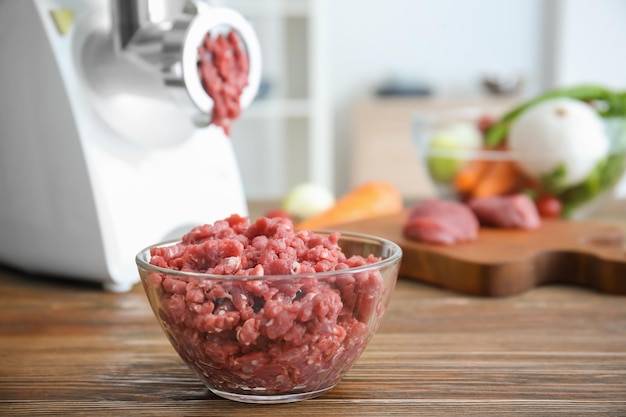 Picadora de carne con carne fresca en la mesa de la cocina