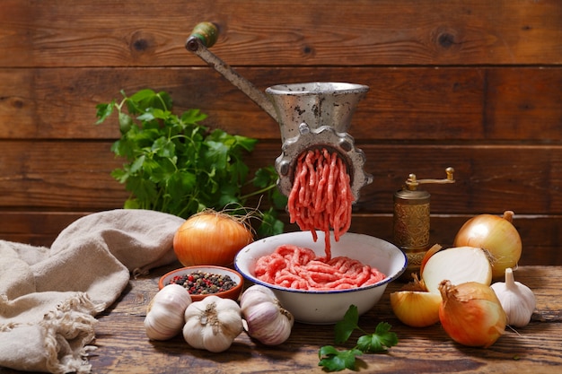 Picadora de carne vieja con carne picada y verduras en la mesa de madera