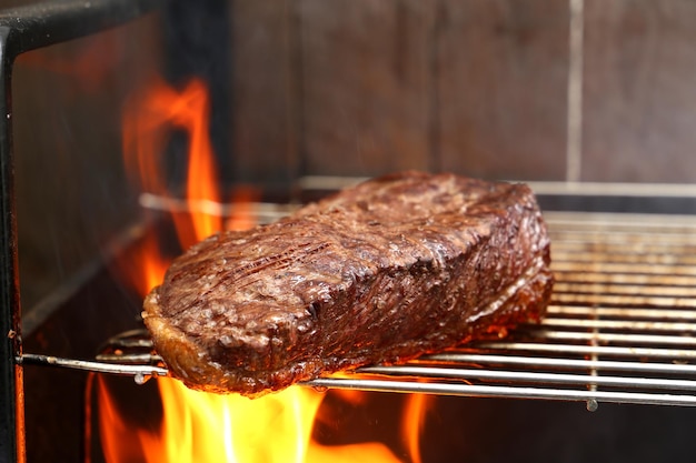 Picanha brasileira no churrasco grelhado no carvão com fundo de madeira e fogo