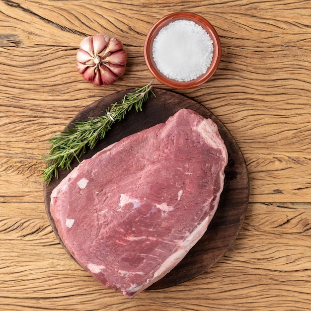 Picanha cruda o carne de rabadilla sobre tabla de madera con condimentos