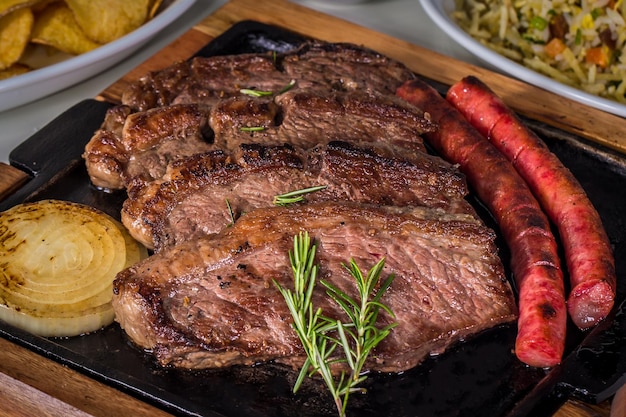 Foto picanha tradicional corte de carne brasileira servido com cebola grelhada e linguiça em uma chapa de ferro quente