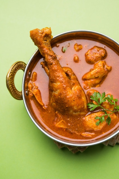 Picante Caril de Frango Avermelhado ou Masala, com Perna proeminente, servido em uma tigela ou Kadhai sobre fundo colorido ou de madeira. foco seletivo.