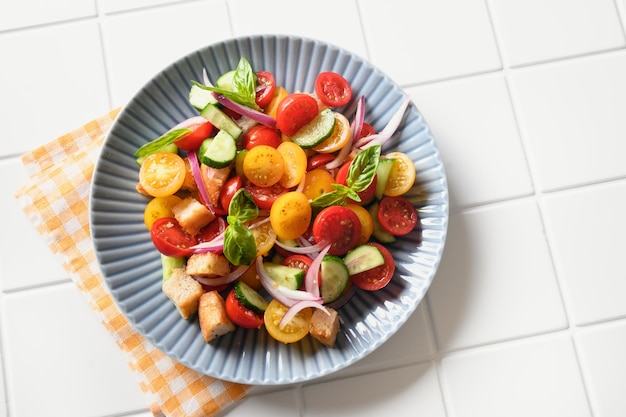 Picante Panzanella com tomate, pão, queijo em prato azul sobre fundo branco da cozinha. Vista do topo. Cozinha italiana. Salada de panzanella vegana colorida de legumes de verão.