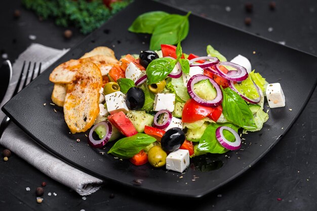 picatostes blancos, con ensalada griega con quesos, en un plato negro, verduras con un paño y madera
