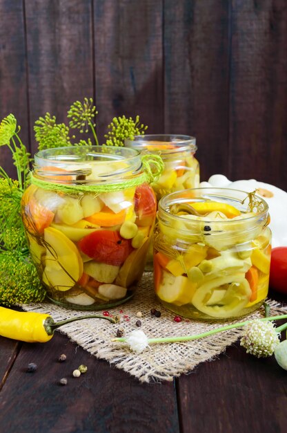 Pickles: variedade de legumes (abobrinha, pimenta, cenoura, tomate, ervilha) em frascos de vidro em uma madeira escura.