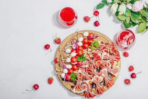 Picknick-Essenskonzept Korb mit Wein und Baguette-Snacks am Spieß Fleisch Käse Gemüse Obst und Blumenstrauß Harte helle dunkle Schatten Steinhintergrund Draufsicht