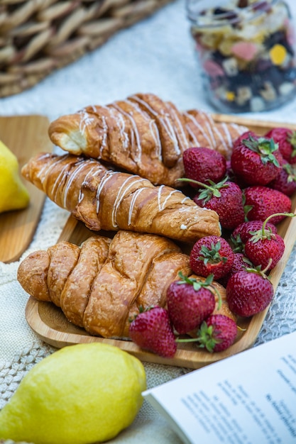 Picknick im Freien in einem üppigen grünen Park mit leckeren Croissantfrüchten, Donuts und Wein auf Gras